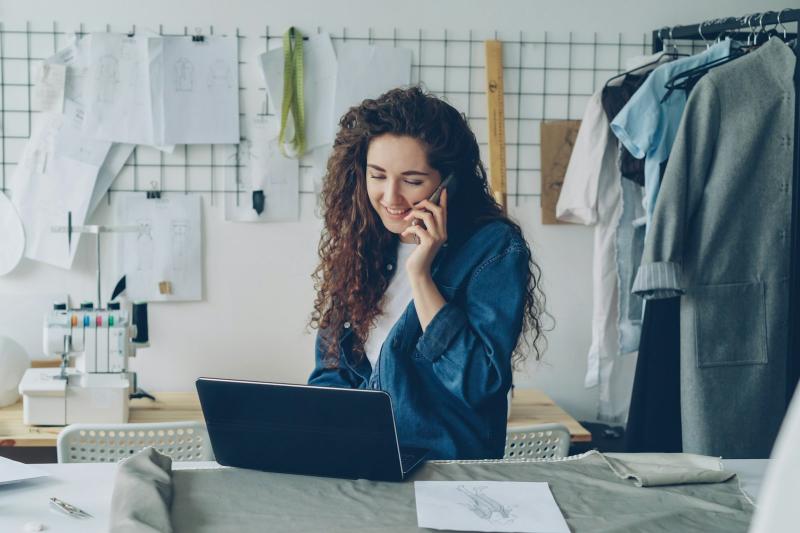 Small business owner on the phone at her laptop in a tailor's workshop, weighing up local SEO cost